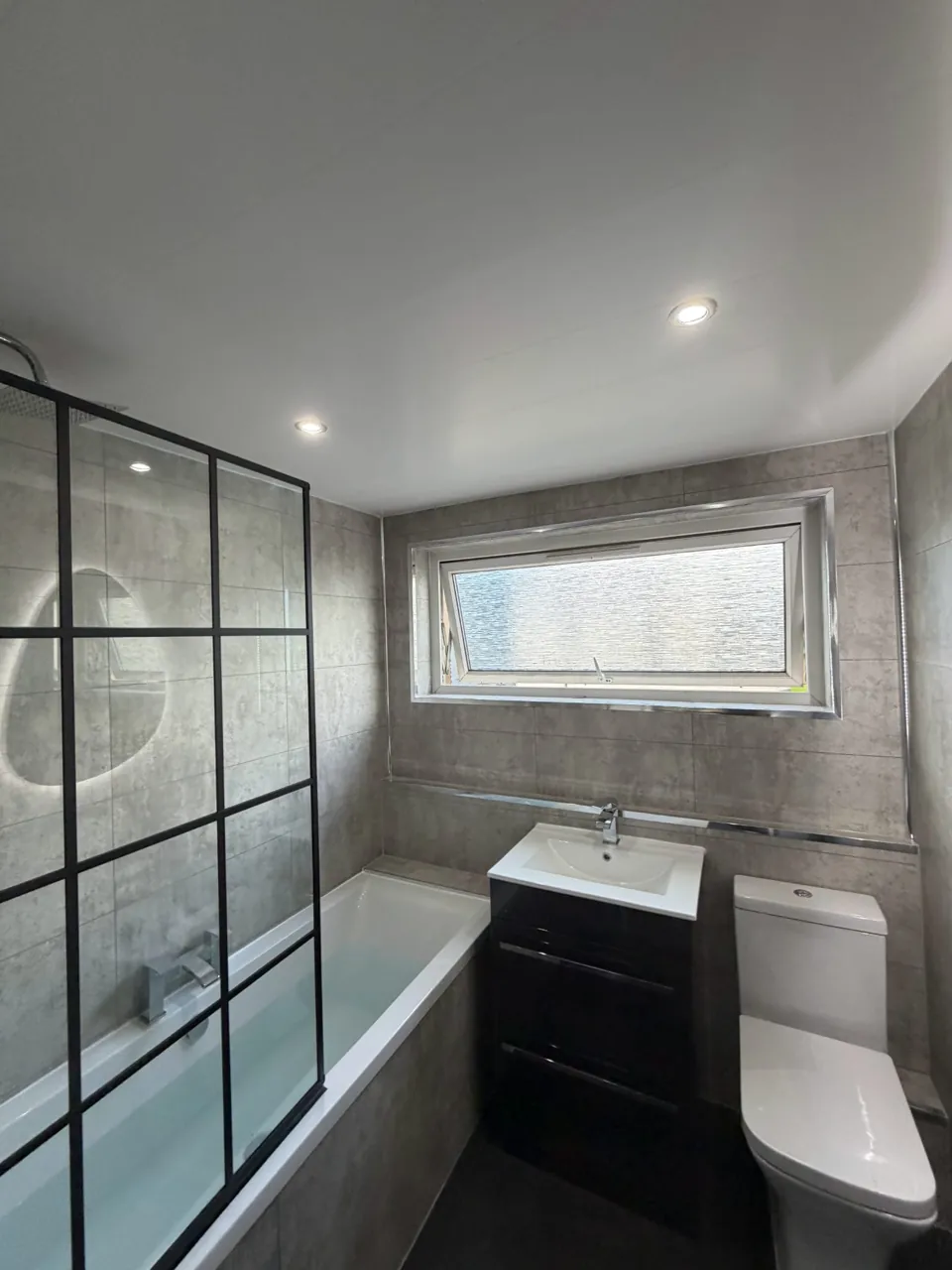 Fitted bath with black shower screen and dark vanity