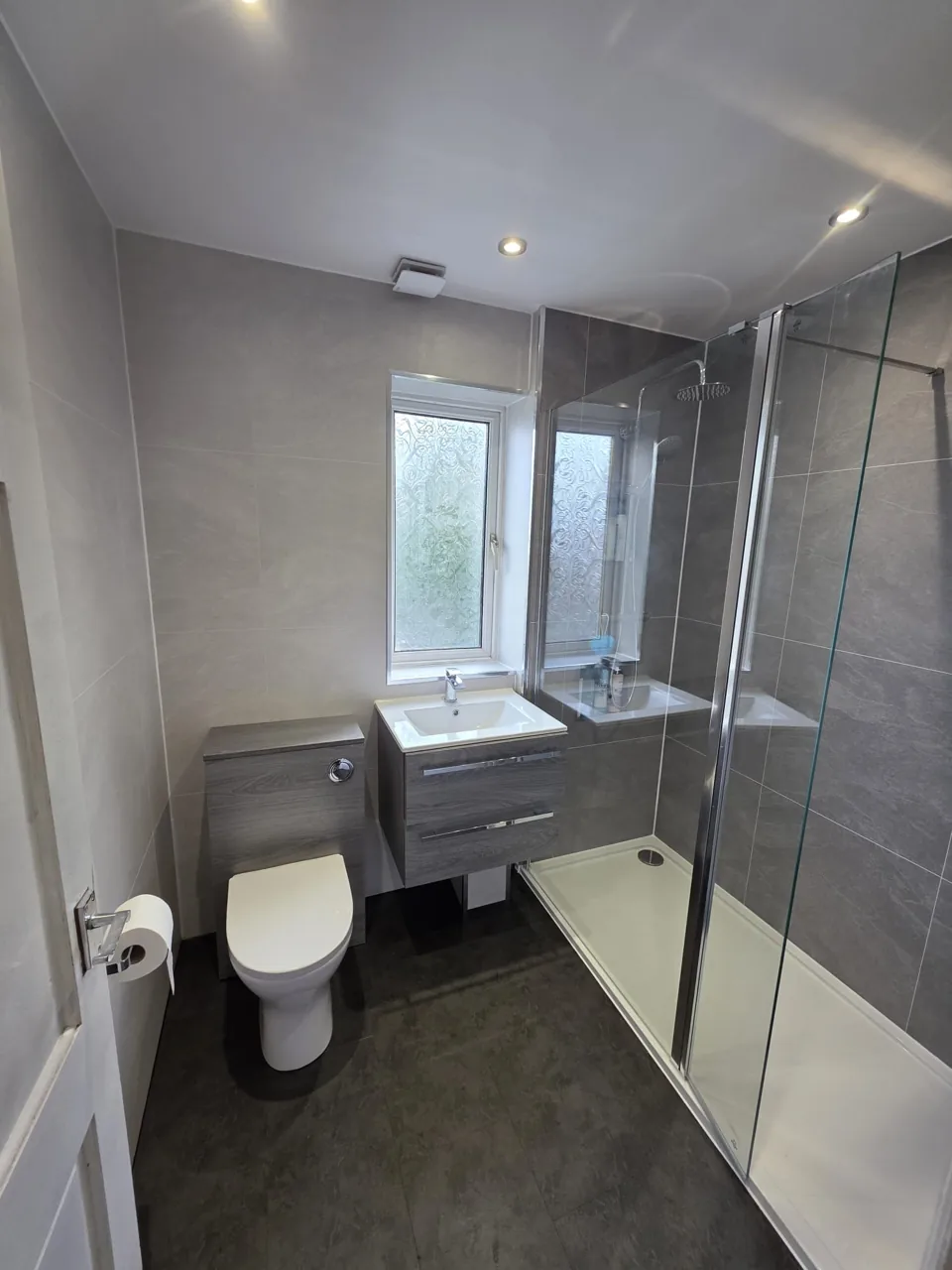 Grey vanity and toilet beside a glass shower screen