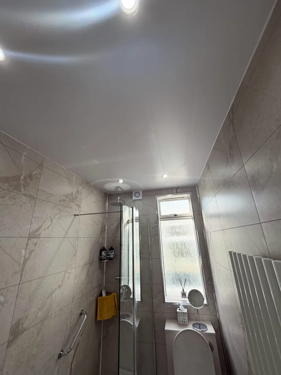 Shower screen and marble-effect walls beneath ceiling lights